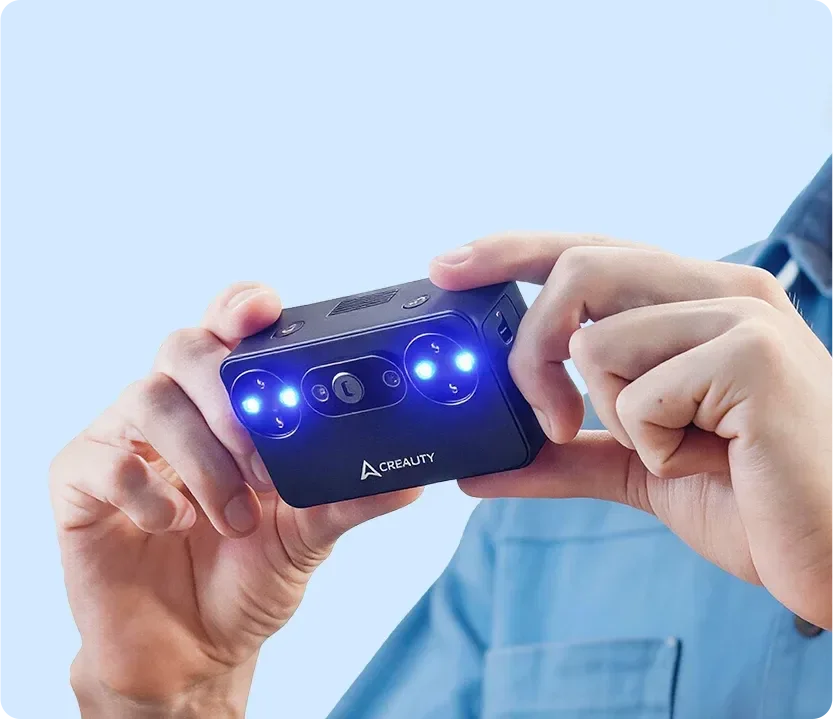Hands holding the Creality Pika handheld 3D scanner with blue lights on